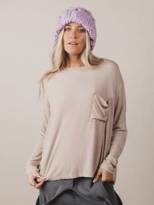 Woman wearing a beige long-sleeve top with a pocket and a purple knitted headband on a plain background