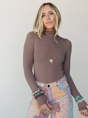 A fitted walnut-toned turtleneck bodysuit styled with patchwork floral jeans and layered boho jewelry — the kind of effortless base layer that makes everything else look intentional.