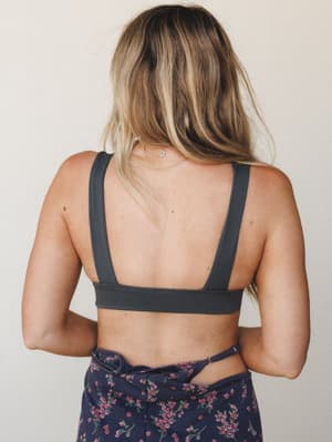 A back-facing shot showing a charcoal bralette with a clean open-back design, paired with a navy floral skirt — the kind of effortless warm-weather outfit that looks like it came together without trying.