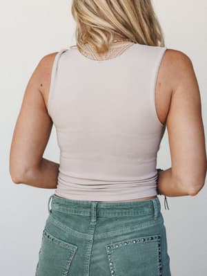 A back-facing shot of a cropped sleeveless tank in soft light taupe, paired with sage green studded corduroy pants — easy, understated, and just the right kind of effortless.