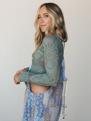 A side-profile shot of a model in a sage green crochet net crop top layered over patchwork floral wide-leg pants, styled against a clean studio backdrop — the mix of textures feels effortlessly collected and free-spirited.