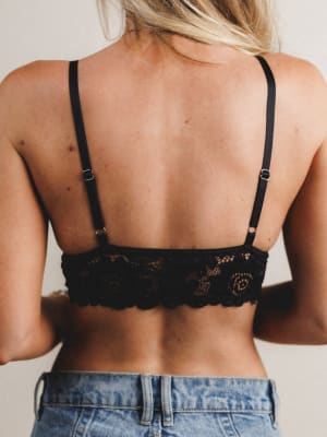 Person wearing a black lace bralette with thin straps and blue jeans.