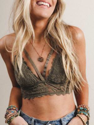 Woman wearing an olive-colored lace bralette with denim shorts against a neutral background