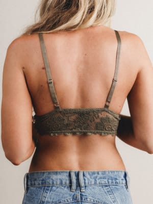 Back view of woman wearing a lace bralette with thin straps and denim shorts on a neutral background