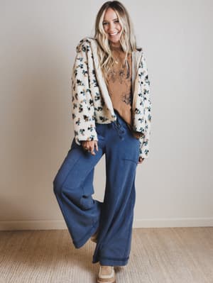 Woman wearing a floral cardigan and blue pants indoors.