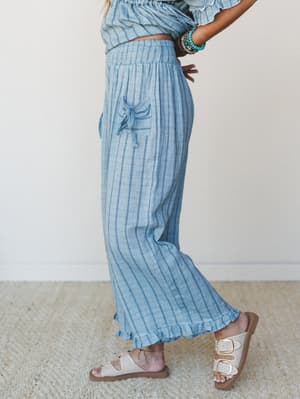 A side-profile shot of wide-leg striped pants in a soft denim blue, styled with a matching cropped top, beaded bracelets, and double-buckle sandals — the kind of easy, put-together set that looks like you tried just enough.