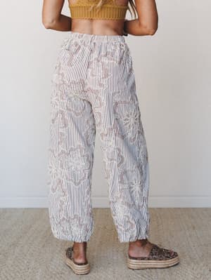 Shot from behind, these wide-leg embroidered pants in a cream and mocha stripe are styled with a mustard knit crop top and leopard platform sandals — relaxed and expressive with just enough texture to feel intentional.