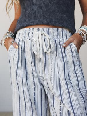 A close-up detail shot of wide-leg striped pants with a smocked drawstring waist, styled with a washed ribbed crop top and stacked beaded bracelets — the kind of easy, put-together look that travels well and feels even better.