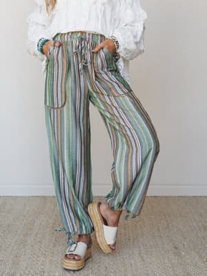 Striped wide-leg pants in a mix of sage, slate, and rust worn with a white eyelet blouse and platform espadrille sandals — the kind of outfit that makes even a Tuesday feel like you're somewhere warm.