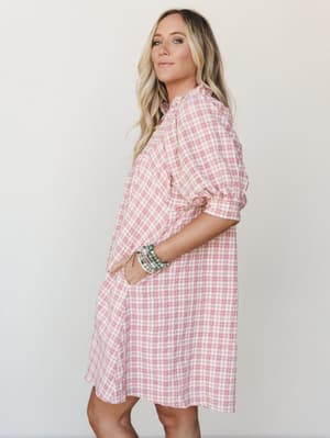 A breezy pink plaid mini dress with ruffle neckline and puff sleeves, styled with stacked beaded bracelets — the kind of dress that makes a Tuesday feel like a little occasion.