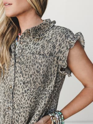 A close-up detail shot of a leopard print denim dress with ruffle trim sleeves and a chest pocket, styled with layered beaded bracelets and a colorful beaded necklace — that perfect mix of wild print and feminine softness.