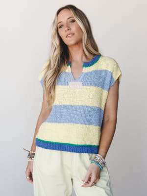 A breezy knit sweater top in bold butter yellow and periwinkle stripes styled with matching pale yellow trousers and stacked bead bracelets — casual and colorful with a laid-back, summery feel.
