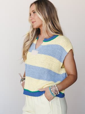 A breezy striped knit top in buttery yellow and periwinkle with green trim details, styled with soft cream trousers and stacked beaded bracelets — the kind of outfit that makes a Tuesday feel like a beach town.