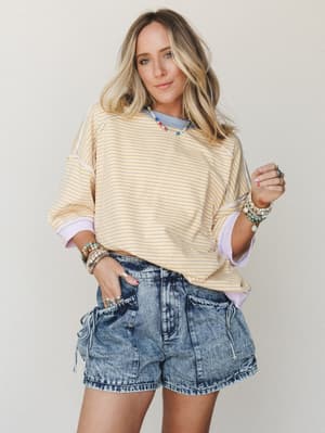 A breezy, lived-in summer look — oversized yellow stripe sweatshirt layered over a blue tee, paired with acid wash denim cargo shorts and stacked with colorful beaded jewelry for that effortless, collected feel.