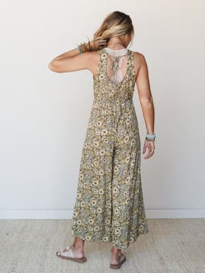 A floral wide-leg jumpsuit shot from behind, showing off its lace-inset open back and relaxed silhouette — the kind of piece that looks effortless on a summer Saturday.
