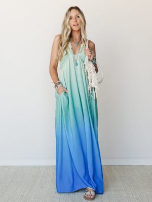 A flowy ombre maxi dress transitions from soft mint at the top to vivid cobalt blue at the hem, styled with layered turquoise jewelry, a macrame fringe bag, and flat sandals for an effortlessly free-spirited warm-weather look.