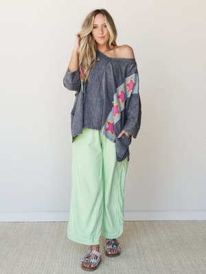 An oversized acid-wash top with diagonal star appliqué detail is styled with wide-leg mint green pants and embellished sandals — the kind of outfit that looks effortless but is clearly doing a lot.
