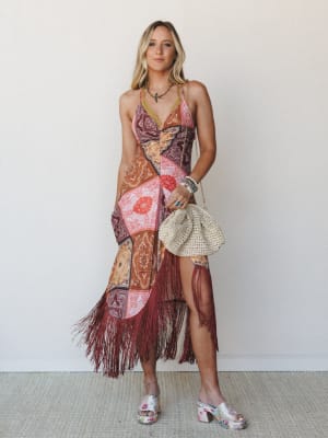 A patchwork bandana-print midi dress with deep burgundy fringe hem styled with a woven clutch, layered jewelry, and floral platform mules — the kind of outfit that has a whole personality.
