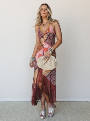 A patchwork maxi dress in warm burgundy and coral tones with long fringe hem styling — the kind of dress that looks equally at home at a summer concert or golden hour dinner.