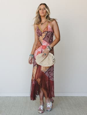 A patchwork maxi dress in warm burgundy and coral tones with long fringe hem styling — the kind of dress that looks equally at home at a summer concert or golden hour dinner.