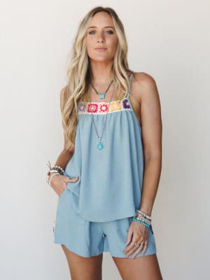A flowy dusty blue matching set — crochet-trimmed tank and mini shorts — styled with turquoise jewelry and stacked bracelets for a laid-back boho feel that's equal parts beach-ready and effortlessly put-together.