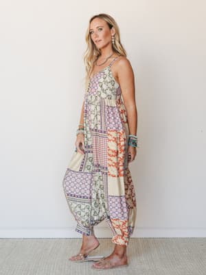 A flowy patchwork jumpsuit in warm earthy tones shot against a clean studio wall — the kind of piece that looks like it was made from every beautiful fabric you've collected over the years.