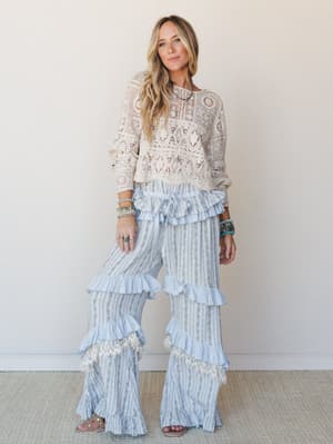 A full-body studio shot of a model in a cream crochet crop top paired with wide-leg ruffle flare pants in a soft blue stripe and floral print — the kind of outfit that makes Saturday feel like a whole mood.