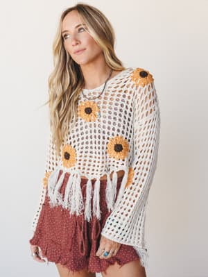 A cropped open-knit crochet top with sunflower appliqués and fringe hem, styled over a terracotta floral mini skort — the kind of outfit that looks like it was made for a long summer day with nowhere specific to be.