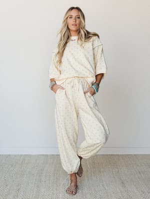 A matching polka dot two-piece set in soft butter yellow with powder blue dot print and contrast piping — styled with stacked turquoise bracelets and strappy sandals for a relaxed, pulled-together feel that reads effortlessly comfortable.