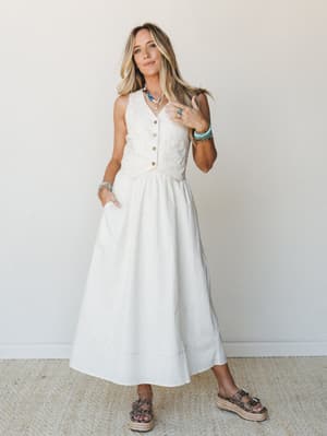 A cream linen-look midi dress with a structured button-front bodice and full A-line skirt, styled with turquoise jewelry and espadrille platform sandals — the kind of outfit that works just as hard at a farmers market as it does at a bridal shower.