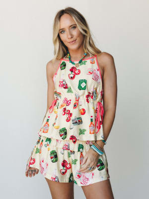 A fun, conversation-starting matching set in a cream novelty print featuring tomatoes, Tabasco bottles, and garden vegetables — styled with stacked colorful bracelets and a beaded necklace for a playful, summer-ready look.