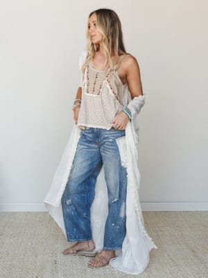 A breezy, layered look — embroidered cami, flowy white duster, and lived-in wide-leg jeans styled with stacked turquoise bracelets and slide sandals, shot against a clean indoor wall with that effortless 'just threw this on and it worked' energy.