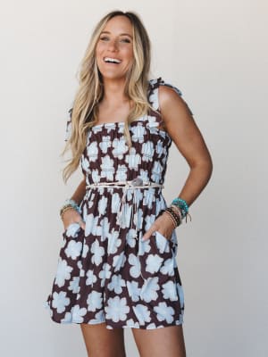 A smocked mini dress in a bold brown and sky blue oversized floral print, styled with a delicate braided belt and stacked boho bracelets — the kind of outfit that looks like you planned it but wore it because it felt good.