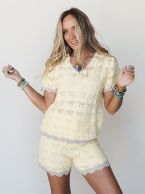 A bright, breezy two-piece knit set in soft butter yellow with contrast lavender trim — worn with stacked boho bracelets and a statement necklace, the whole look has that effortless 'grabbed it off the chair and it worked' energy.