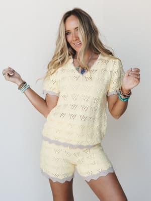 A bright, breezy two-piece knit set in soft butter yellow with contrast lavender trim — worn with stacked boho bracelets and a statement necklace, the whole look has that effortless 'grabbed it off the chair and it worked' energy.