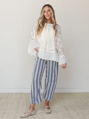 A lace bell-sleeve top paired with wide-leg striped crop pants in a clean studio setting — the kind of outfit that reads effortlessly put-together without trying too hard.