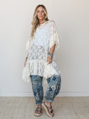 A sheer cream lace tunic layered over a white cami is paired with floral-printed denim joggers and studded espadrille sandals — the kind of outfit that feels effortlessly put-together without trying too hard.