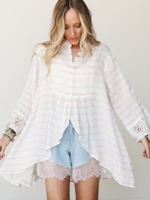 A breezy, oversized striped linen button-down with flowy high-low hem and floral-cuffed sleeves is paired with light wash denim shorts trimmed in scalloped lace — soft, romantic, and completely wearable.