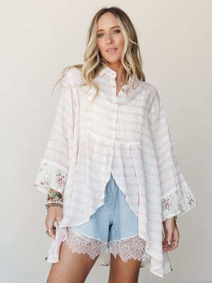 An oversized striped button-down with floral-contrast cuffs and a handkerchief hem is paired with light denim shorts finished in lace trim — soft, laid-back, and just the right amount of romantic.