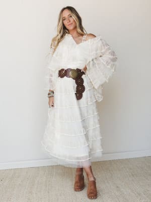 A dreamy, all-ivory tiered ruffle dress styled with a chunky brown leather concho belt and suede mules — romantic boho energy that walks the line between bridal and festival without trying too hard.