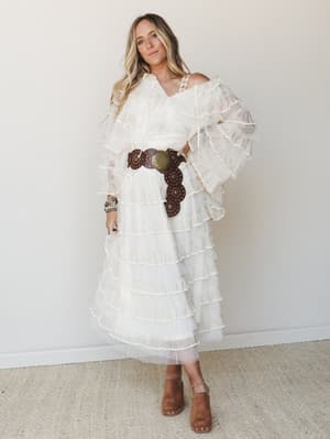 A dreamy, all-ivory tiered ruffle dress styled with a chunky brown leather concho belt and suede mules — romantic boho energy that walks the line between bridal and festival without trying too hard.