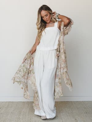 A breezy all-white cami-and-wide-leg-pants set layered under a flowing floral-patchwork kimono duster, styled with stacked bracelets and a beaded necklace for that effortless, collected boho feel.