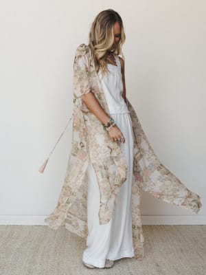 A flowy maxi kimono in a soft patchwork floral print billows open over a white linen tank and wide-leg pants — the kind of layered, effortless outfit that looks like it happened naturally but definitely didn't.