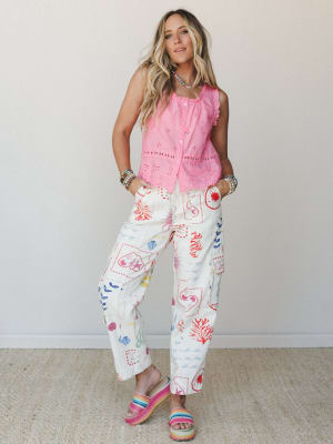 A full-body model shot pairing a bright pink eyelet button-front tank with wide-leg cream pants covered in a playful multicolor ocean-themed print — finished with rainbow platform sandals and stacked bead bracelets for a summer-ready, colorful boho f