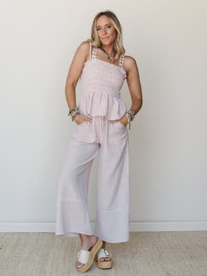 A smocked, ruffle-hem top and wide-leg striped pants set in soft blush pink, styled with stacked beaded bracelets, a colorful beaded necklace, and white platform espadrilles — the kind of outfit that works just as hard at brunch as it does at the far