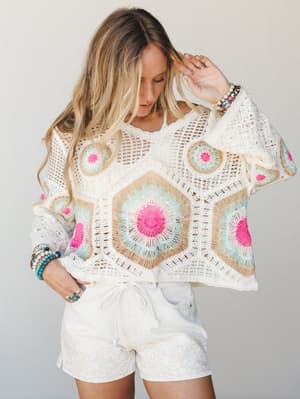 A breezy crochet granny square top in cream with pops of hot pink and mint is paired with textured white shorts — the kind of outfit that makes a Tuesday feel like a vacation.