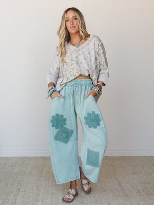 A relaxed, feel-good outfit pairing — wide-leg mint pants with crochet patchwork appliqués meet a flowy floral crop sweatshirt, styled with stacked bracelets and sandals for that effortlessly lived-in boho look.