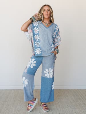 A matching two-piece set in heathered blue with oversized daisy print panels — worn with stacked boho bracelets and rainbow platform sandals, the whole look has a retro-easy, free-spirited energy that feels just as at home at brunch as it does at a s
