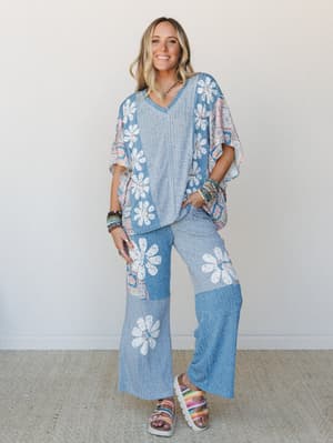 A matching two-piece set in heathered blue with bold white daisy appliqués — the relaxed poncho top and wide-leg flare pants feel like a full outfit that came together effortlessly, styled with stacked bracelets and colorful platform sandals against