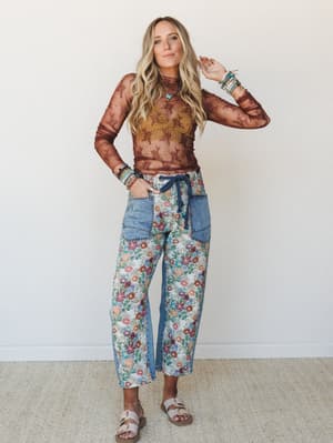 A breezy, texture-rich outfit pairing a sheer brown lace long-sleeve top over a mustard bralette with wide-leg floral-and-denim patchwork pants — the kind of layered boho look that feels intentional without trying too hard.
